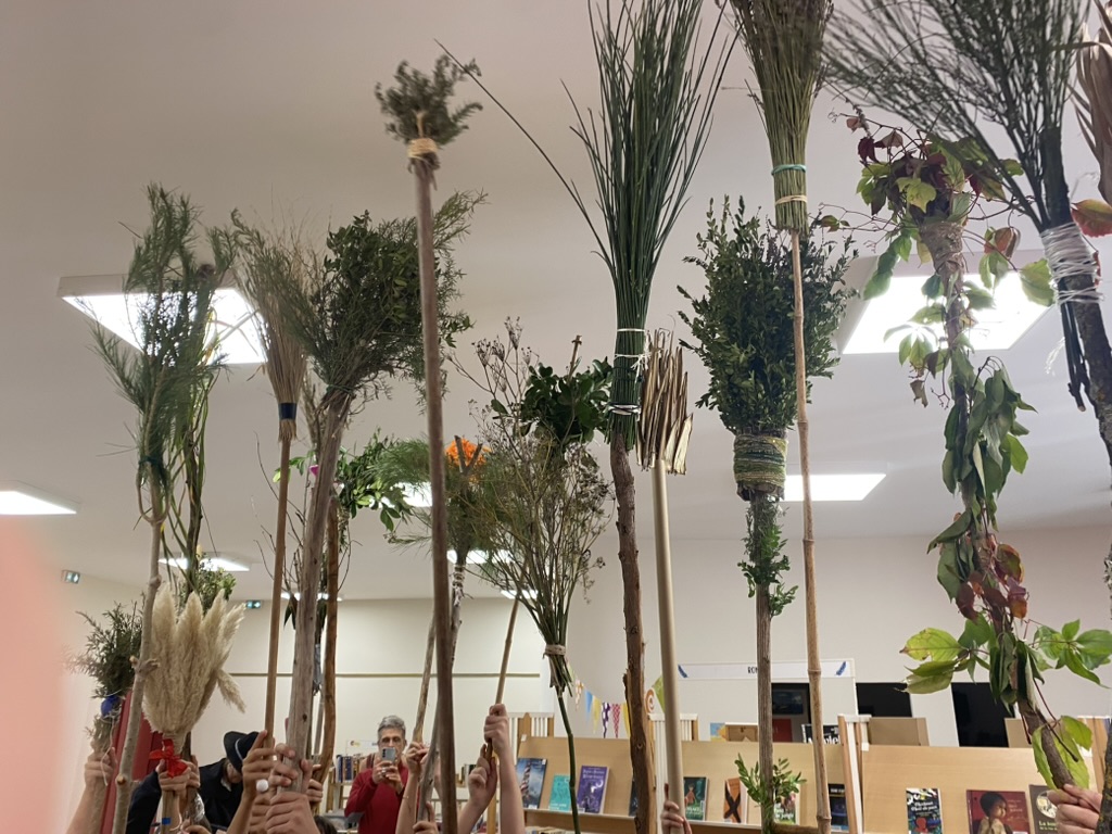 Des enfants brandissent des balais de sorcière fabriqués avec des branchages, dans une médiathèque