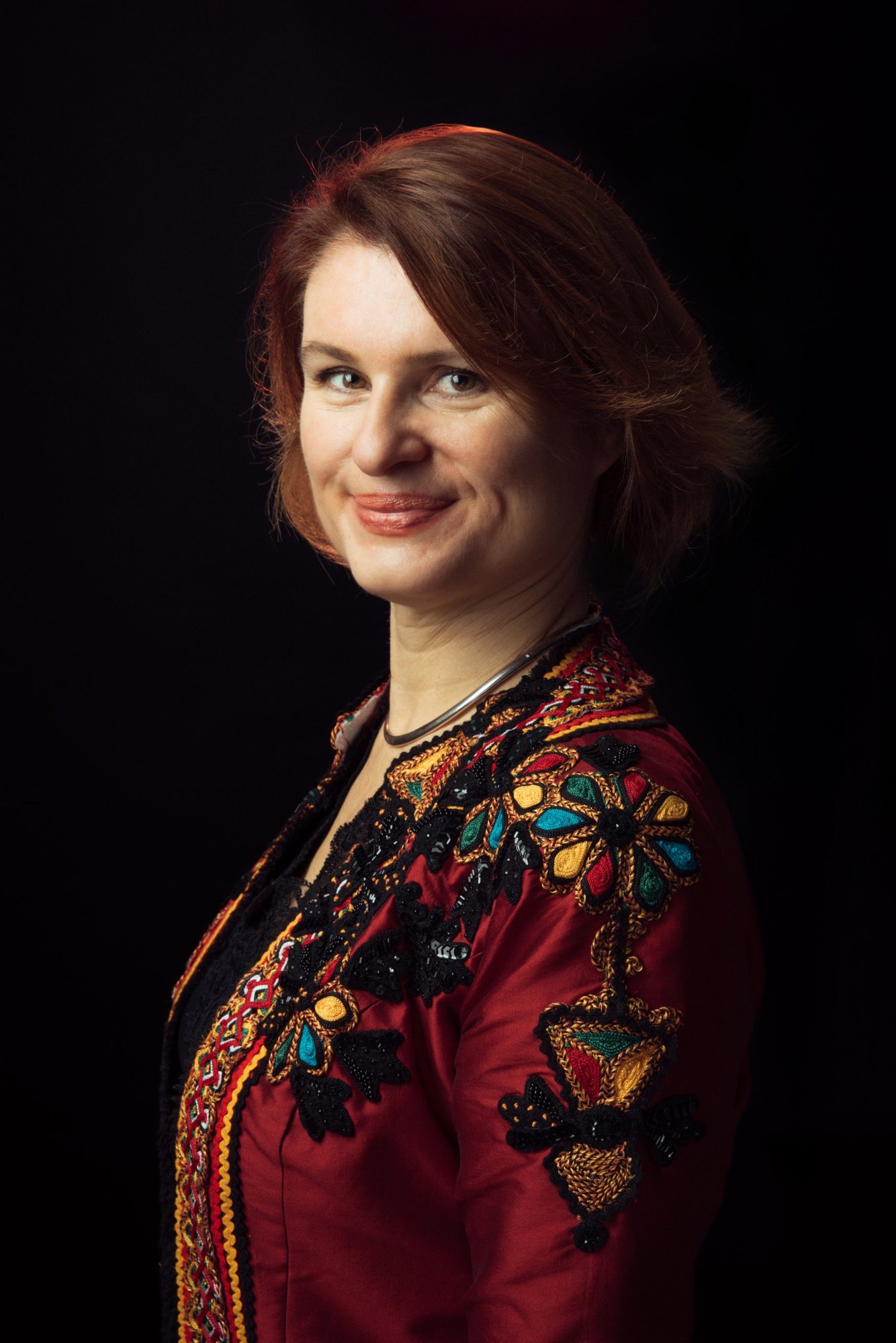 Portrait d’Audrey Alwett de trois quarts, veste rouge brodée, sur fond noir